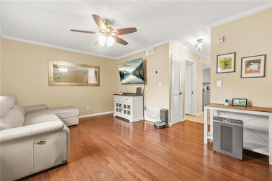 Living room with a ceiling fan, wood finished floors, crown molding, and baseboards