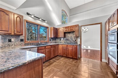 Kitchen with brown cabinets, healthy amount of natural light, dark stone counters, and high vaulted ceiling