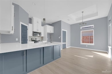 Kitchen featuring white cabinets, backsplash, decorative light fixtures, and stainless steel appliances