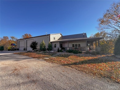 View of front of property featuring stone siding, covered porch, driveway, and a metal roof