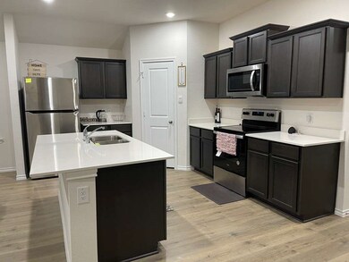 Kitchen with appliances with stainless steel finishes, light wood-style floors, a kitchen island with sink, dark cabinetry, and recessed lighting
