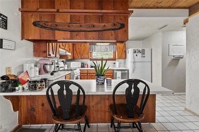 Kitchen featuring white appliances, under cabinet range hood, a peninsula, light countertops, and brown cabinetry