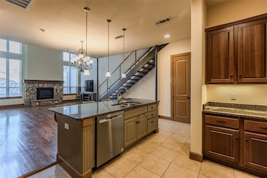 Kitchen featuring a stone fireplace, decorative light fixtures, stainless steel dishwasher, a center island with sink, and dark stone countertops