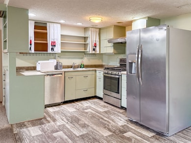 Basement kitchen with stainless steel appliances, light countertops, a textured ceiling, light wood-type flooring, and under cabinet range hood