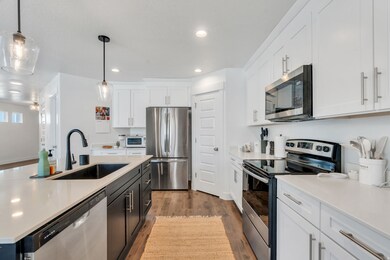 Kitchen with appliances with stainless steel finishes, light wood-style floors, white cabinetry, hanging light fixtures, and a kitchen island with sink