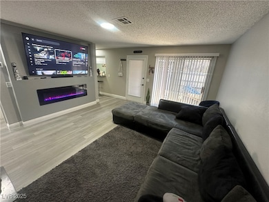 Living room with wood finished floors, a textured ceiling, and a glass covered fireplace
