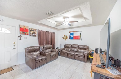 Tiled living room with a tray ceiling, a textured ceiling, and ceiling fan