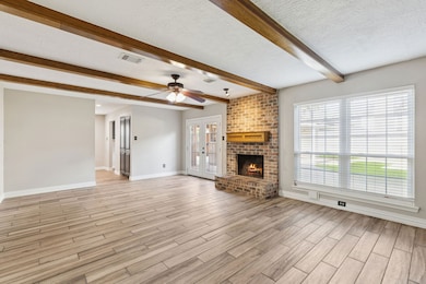 Discover the heart of the home in this living area where fresh paint, high ceilings, exposed wood beams, and a striking brick fireplace come together to create a warm and inviting gathering space.
