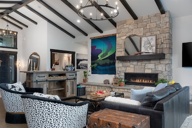 Living area featuring a chandelier, a stone fireplace, beamed ceiling, and high vaulted ceiling