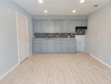 Kitchen with tasteful backsplash, under cabinet range hood, light wood-style flooring, baseboards, and recessed lighting