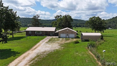 View of front of home featuring dirt driveway, an outdoor structure, a front lawn, a view of rural / pastoral area, and a metal roof