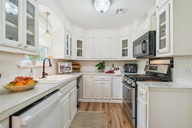 Kitchen with gas range, black microwave, dishwasher, and white cabinetry