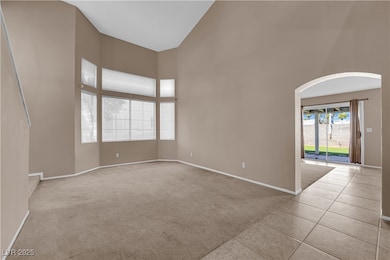 Empty room with high vaulted ceiling, light colored carpet, light tile patterned floors, and arched walkways