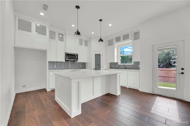 Kitchen featuring backsplash, light countertops, stainless steel microwave, a center island, and white cabinetry
