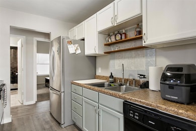 Kitchen with sink, white cabinetry, black dishwasher, hardwood / wood-style floors, and decorative backsplash