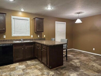 Kitchen with dark countertops, a peninsula, a kitchen bar, dark brown cabinets, and black dishwasher