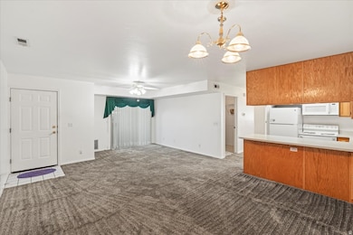 Kitchen featuring white appliances, pendant lighting, a peninsula, light countertops, and brown cabinetry