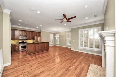Open-concept living space featuring hardwood floors and a modern kitchen with stainless steel appliances and rich wood cabinetry. Large windows fill the room with natural light and offer views of the backyard