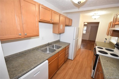 Kitchen featuring white appliances, light wood-type flooring, dark countertops, a textured ceiling, and under cabinet range hood