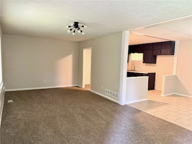 Unfurnished living room featuring a sink, baseboards, a textured ceiling, light tile patterned floors, and light carpet