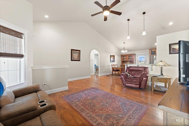 Living area with a ceiling fan, arched walkways, plenty of natural light, wood finished floors, and high vaulted ceiling