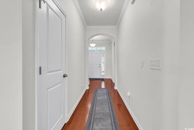 Hallway with arched walkways, dark wood-type flooring, ornamental molding, and baseboards