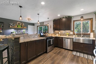 Kitchen with dark brown cabinets, a peninsula, appliances with stainless steel finishes, light stone counters, and dark wood-style floors