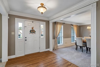Carpeted entrance foyer featurinornamental molding, wood finished floors, wainscoting, and a chandelier