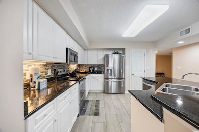 Kitchen featuring appliances with stainless steel finishes, backsplash, dark stone counters, white cabinetry, and a textured ceiling
