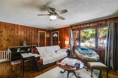 Living area featuring ceiling fan, a textured ceiling, wood walls, and wood finished floors