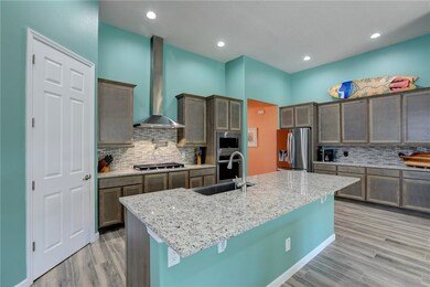 Kitchen with light stone countertops, tasteful backsplash, light wood-style flooring, wall chimney exhaust hood, and stainless steel appliances
