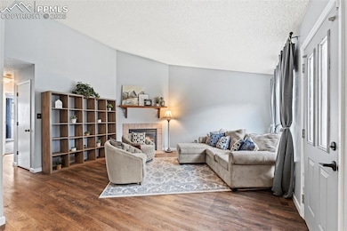 Living room featuring wood finished floors, a textured ceiling, a tiled fireplace, and lofted ceiling
