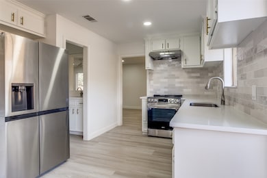 Kitchen featuring appliances with stainless steel finishes, backsplash, white cabinets, under cabinet range hood, and light wood-type flooring