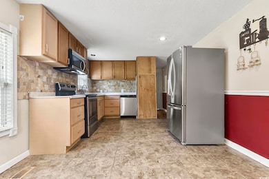 Kitchen with stainless steel appliances, light countertops, backsplash, a textured ceiling, and recessed lighting