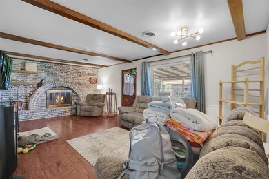 Living room featuring beamed ceiling, wood finished floors, a chandelier, and a brick fireplace
