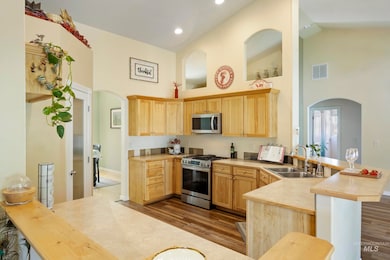 Kitchen featuring appliances with stainless steel finishes, high vaulted ceiling, arched walkways, a peninsula, and light brown cabinets