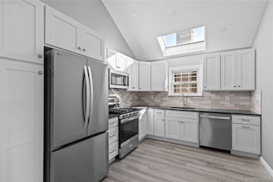 Kitchen featuring appliances with stainless steel finishes, white cabinetry, backsplash, a skylight, and light wood-type flooring