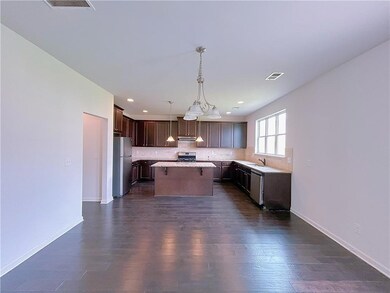 Kitchen with dark brown cabinetry, a kitchen island, hanging light fixtures, dark wood-style flooring, and stainless steel appliances