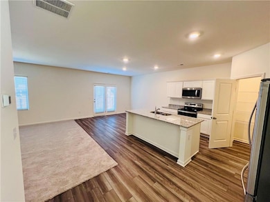 Kitchen featuring appliances with stainless steel finishes, sink, light stone counters, white cabinetry, and a kitchen island with sink