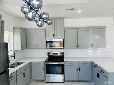 Kitchen featuring appliances with stainless steel finishes, a sink, light marble finish flooring, gray cabinets, and light countertops