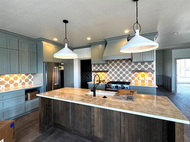 Kitchen with decorative backsplash, high end black fridge, premium range hood, pendant lighting, and light stone counters