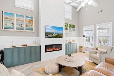 Living room with a ceiling fan, light wood finished floors, a fireplace, visible vents, and a towering ceiling