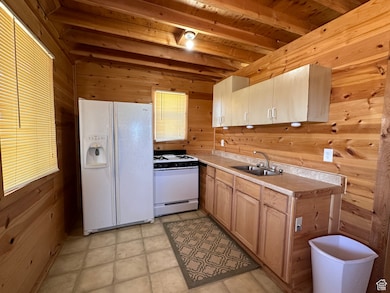 Kitchen with white appliances, wooden walls, sink, beam ceiling, and light brown cabinets