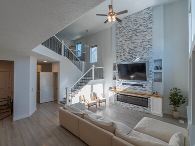 Living room with wood finished floors, a towering ceiling, stairs, a stone fireplace, and ceiling fan
