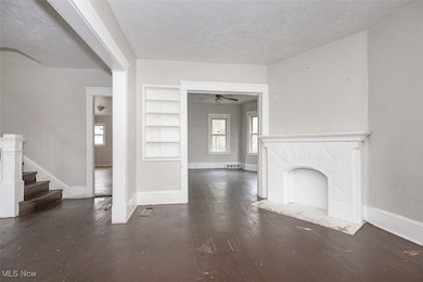 Unfurnished living room with dark wood-style flooring, a textured ceiling, a premium fireplace, built in shelves, and a ceiling fan