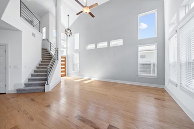 Unfurnished living room featuring stairway, light wood-style flooring, high vaulted ceiling, a ceiling fan, and healthy amount of natural light