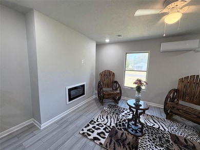 Living area with wood tiled floors, a textured ceiling, a glass covered fireplace, a wall mounted air conditioner, and ceiling fan