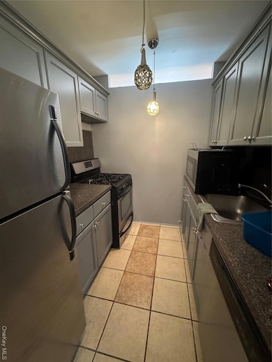 Kitchen featuring gray cabinetry, stainless steel fridge, stove, and pendant lighting