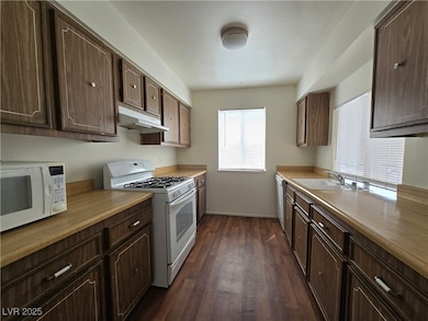 Kitchen featuring white appliances, dark wood-style floors, dark brown cabinetry, under cabinet range hood, and light countertops