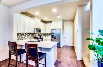 Kitchen featuring stainless steel appliances, decorative backsplash, dark wood-style floors, a kitchen bar, and white cabinets